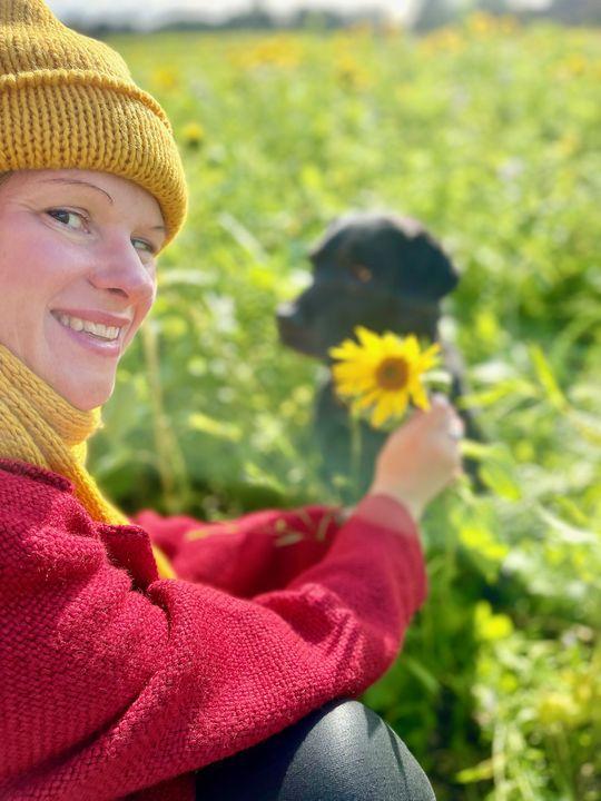 Elkline und Nachhaltigkeit: Der rote Mantel, die gelbe Strickware und der schwarze Labrador machen sich gut im Sonnenblumenfeld, oder?